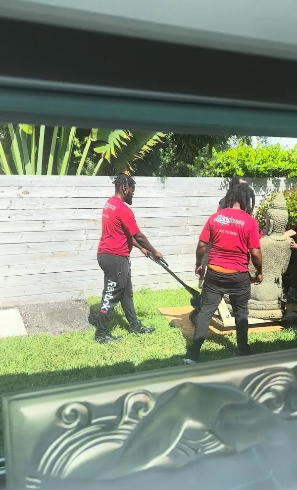 Two Nationwide movers moving a heavy stone statue across a lawn