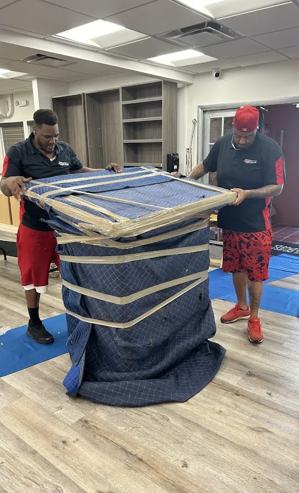 Two Nationwide movers wrapping a large item in blue moving blankets